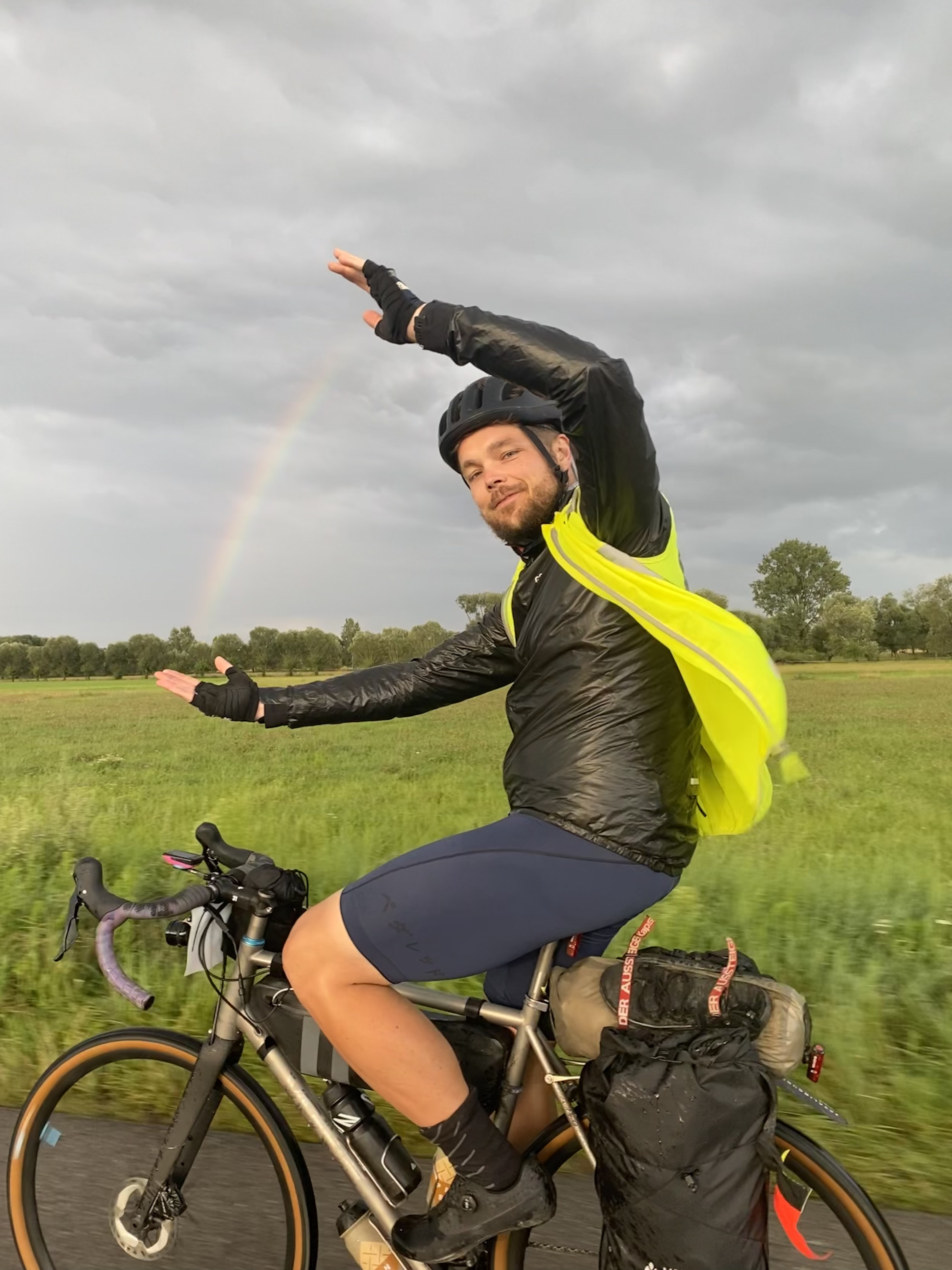 Daniel Hülsewig auf dem Fahrrad mit einem Regenbogen im Hintergrund