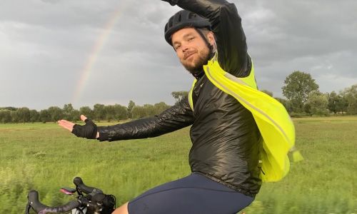 Teaser - Daniel Hülsewig auf dem Fahrrad mit einem Regenbogen im Hintergrund